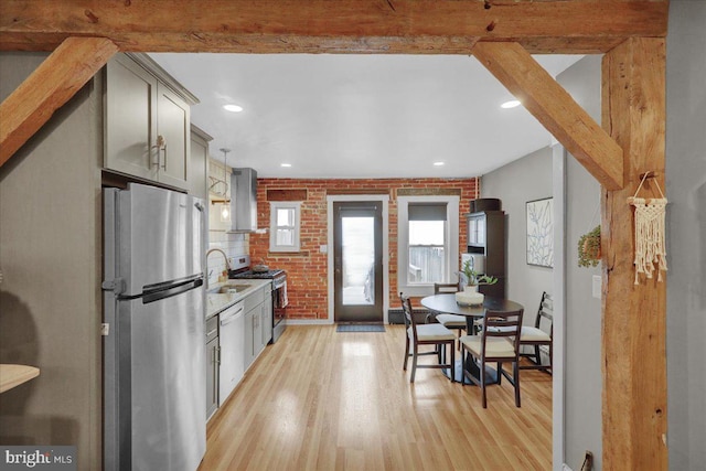 kitchen with brick wall, appliances with stainless steel finishes, beamed ceiling, gray cabinetry, and light wood-type flooring