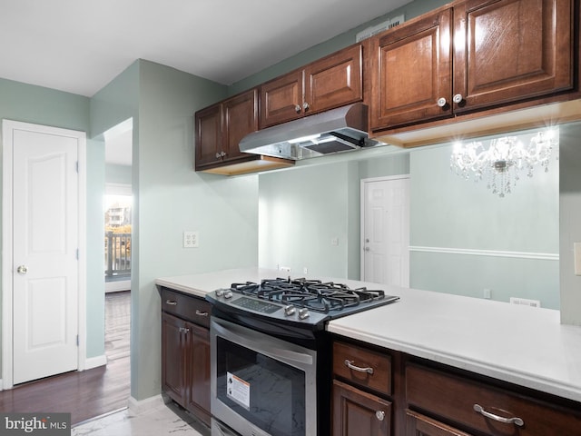 kitchen with baseboards, light countertops, under cabinet range hood, and stainless steel gas range oven