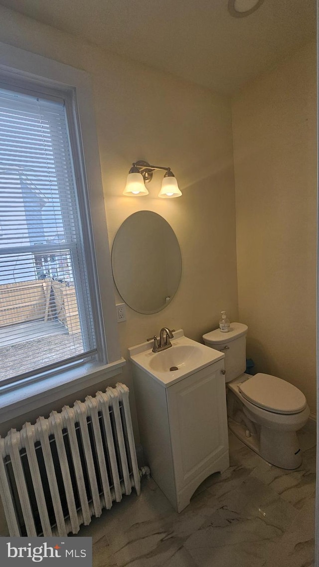 half bathroom with radiator, marble finish floor, toilet, and vanity