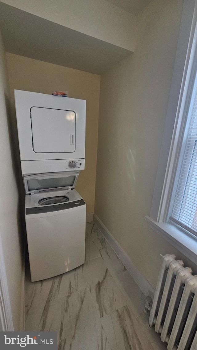 laundry room featuring laundry area, baseboards, radiator, marble finish floor, and stacked washing maching and dryer