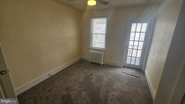 spare room with ceiling fan, radiator heating unit, baseboards, and dark colored carpet