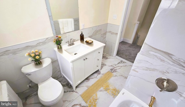 bathroom featuring wainscoting, toilet, a bathing tub, marble finish floor, and vanity