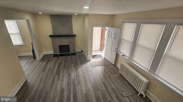 living room with radiator heating unit, a tiled fireplace, baseboards, and dark wood-style flooring