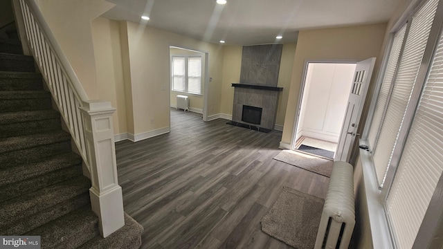 unfurnished living room featuring recessed lighting, a tiled fireplace, radiator heating unit, dark wood-type flooring, and baseboards