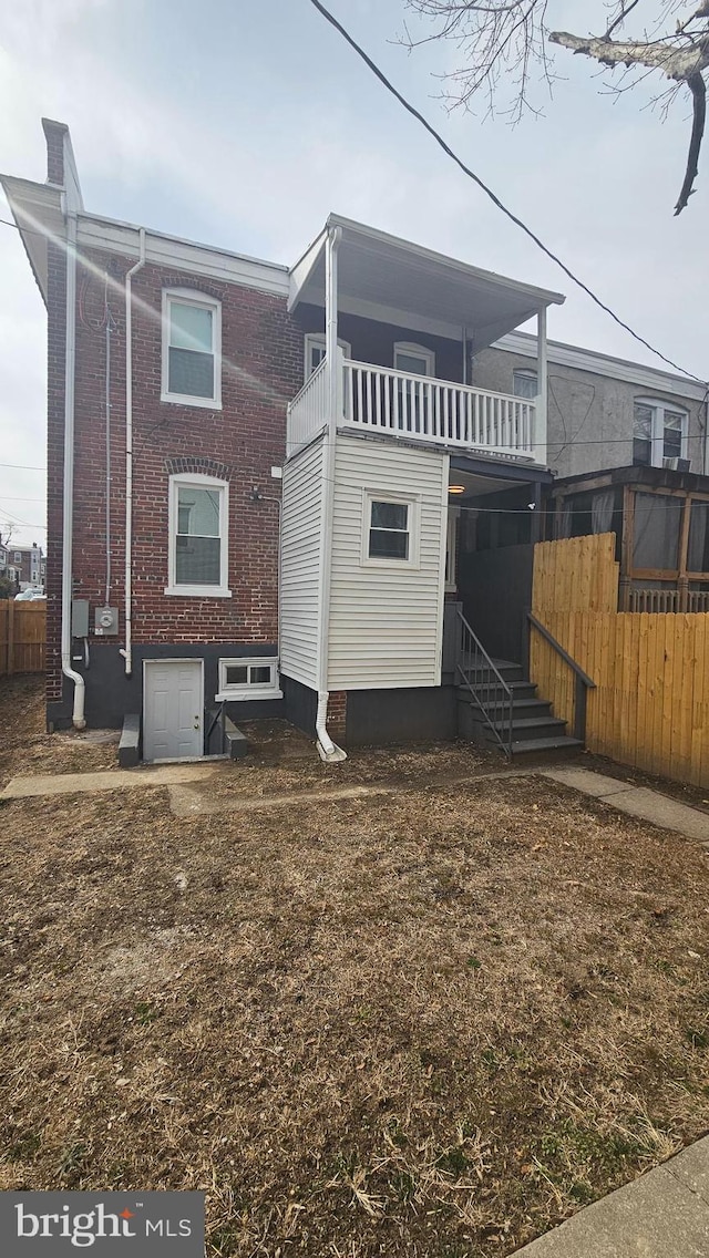 back of property with entry steps, brick siding, fence, and a balcony