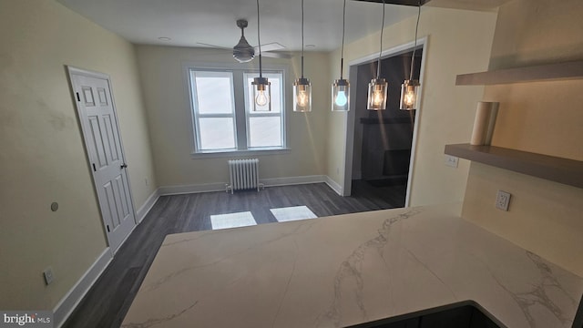 unfurnished dining area featuring ceiling fan, radiator heating unit, dark wood finished floors, and baseboards