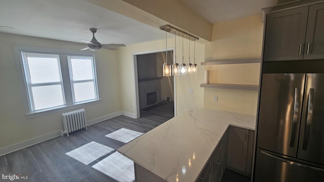 kitchen featuring a fireplace, baseboards, freestanding refrigerator, light stone countertops, and radiator heating unit