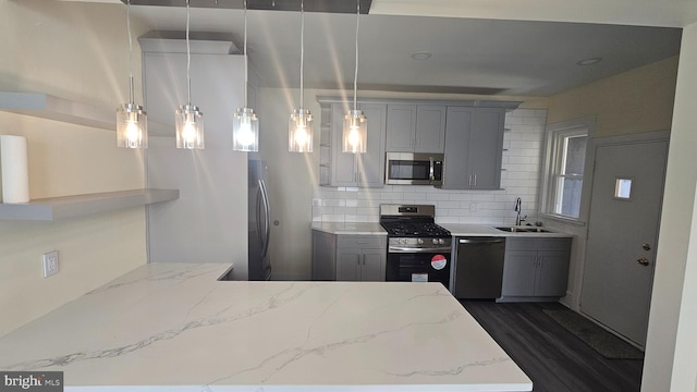 kitchen featuring dark wood-style floors, decorative backsplash, gray cabinetry, appliances with stainless steel finishes, and a sink