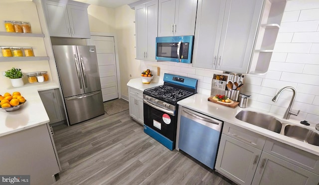 kitchen with open shelves, light countertops, appliances with stainless steel finishes, a sink, and wood finished floors