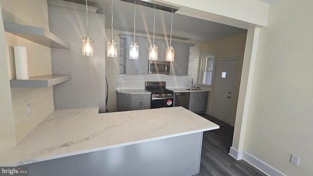 kitchen featuring a peninsula, a sink, appliances with stainless steel finishes, light stone countertops, and tasteful backsplash