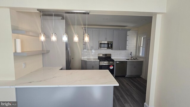 kitchen with stainless steel appliances, a sink, gray cabinets, dark wood-style floors, and tasteful backsplash