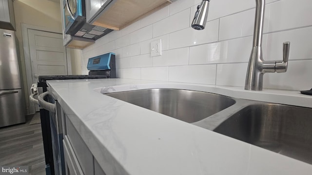 kitchen featuring tasteful backsplash, dark wood finished floors, light stone counters, stainless steel appliances, and a sink