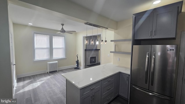 kitchen featuring radiator, light stone counters, freestanding refrigerator, a peninsula, and open shelves