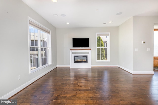 unfurnished living room featuring a glass covered fireplace, recessed lighting, baseboards, and wood-type flooring