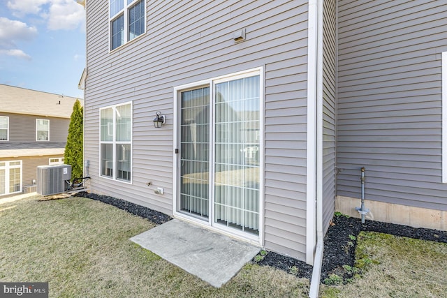 entrance to property featuring central air condition unit and a lawn