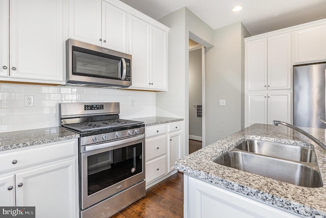 kitchen with a sink, backsplash, white cabinetry, appliances with stainless steel finishes, and dark wood-style flooring