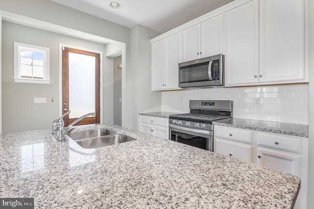 kitchen with a sink, light stone counters, backsplash, appliances with stainless steel finishes, and white cabinets