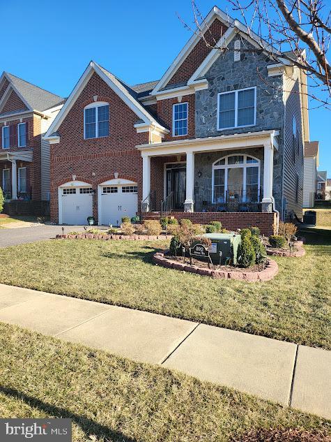 craftsman-style home with brick siding, a porch, a front yard, a garage, and driveway