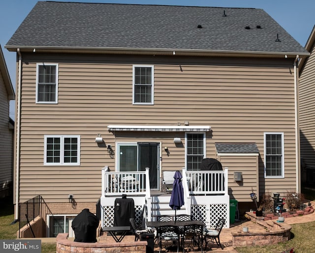 back of property with a shingled roof, a patio area, and a deck