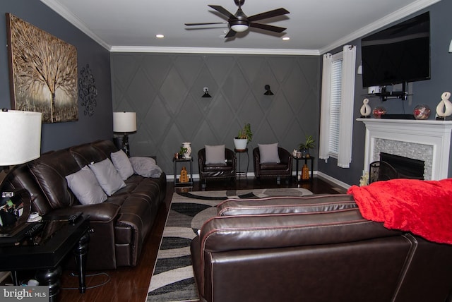 living room featuring ceiling fan, a stone fireplace, wood finished floors, baseboards, and ornamental molding