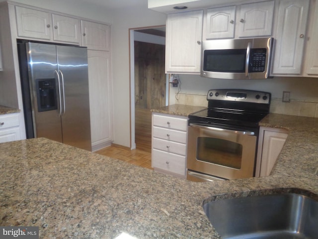 kitchen featuring stainless steel appliances, stone countertops, white cabinets, and a sink