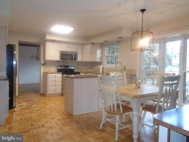 kitchen featuring appliances with stainless steel finishes, white cabinets, decorative light fixtures, and a peninsula