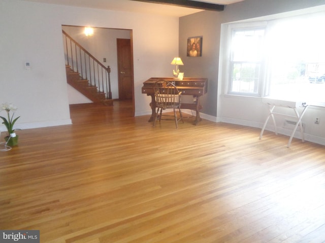 living area featuring stairs, beamed ceiling, baseboards, and light wood-style floors