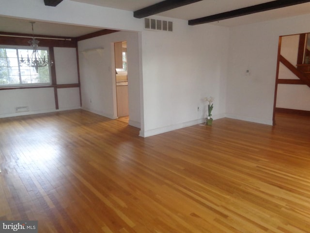 empty room with a chandelier, visible vents, baseboards, light wood-type flooring, and beamed ceiling