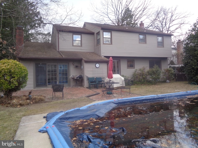 rear view of house with a covered pool, a chimney, and a patio