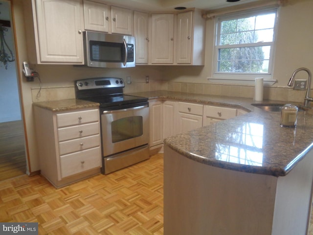 kitchen featuring a peninsula, white cabinets, stainless steel appliances, and a sink