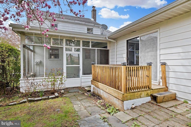 exterior space featuring a sunroom, a chimney, and a wooden deck