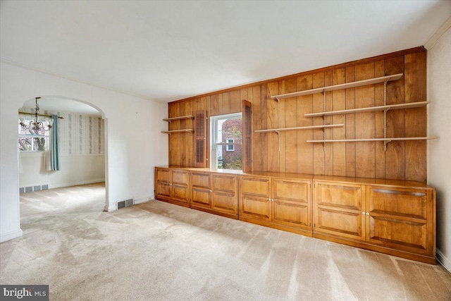 unfurnished living room featuring a notable chandelier, crown molding, light colored carpet, visible vents, and arched walkways