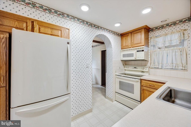 kitchen featuring light countertops, white appliances, wallpapered walls, a sink, and light floors