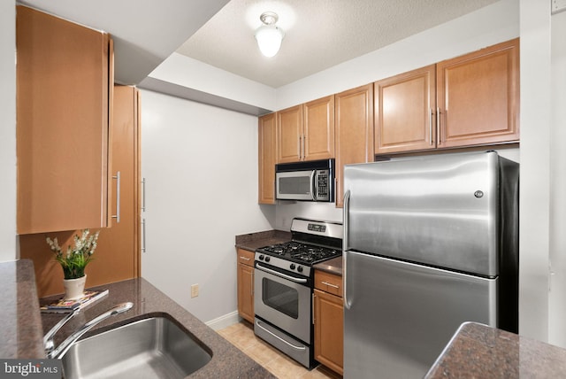kitchen with stainless steel appliances, light tile patterned flooring, a sink, and dark stone countertops