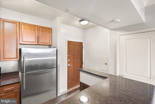 kitchen featuring brown cabinetry, dark stone countertops, and freestanding refrigerator