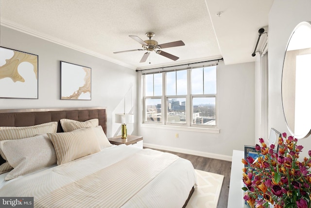 bedroom with a textured ceiling, baseboards, wood finished floors, and crown molding