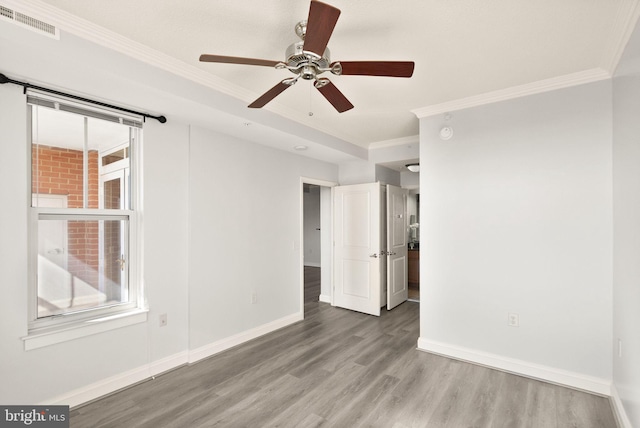 spare room featuring ceiling fan, wood finished floors, visible vents, baseboards, and ornamental molding