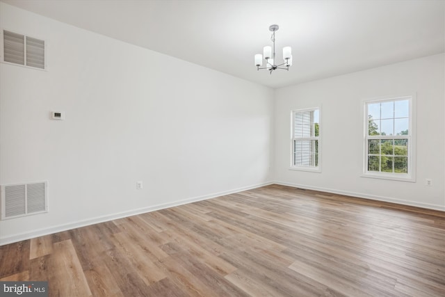 unfurnished room featuring baseboards, light wood-type flooring, visible vents, and an inviting chandelier