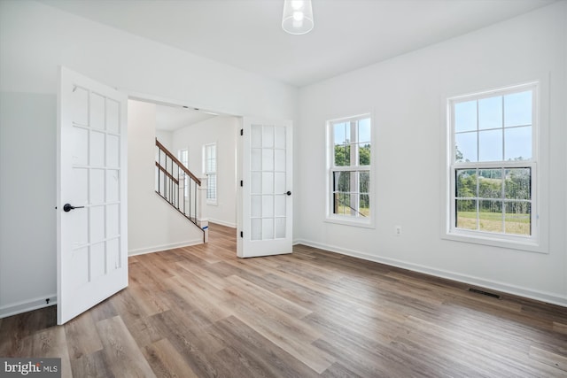 unfurnished room featuring wood finished floors, visible vents, baseboards, and stairs