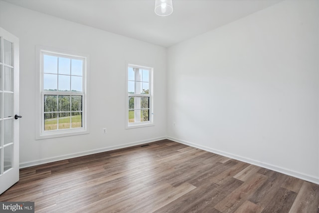 unfurnished room with plenty of natural light, wood finished floors, visible vents, and baseboards