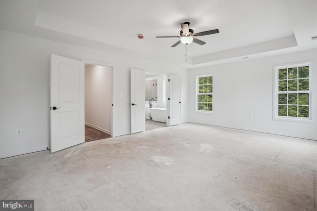 unfurnished bedroom featuring a raised ceiling, connected bathroom, and baseboards