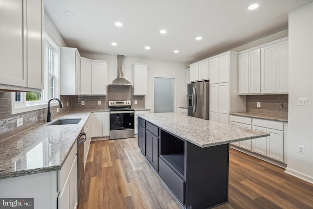 kitchen with stainless steel appliances, wood finished floors, a sink, white cabinets, and wall chimney range hood