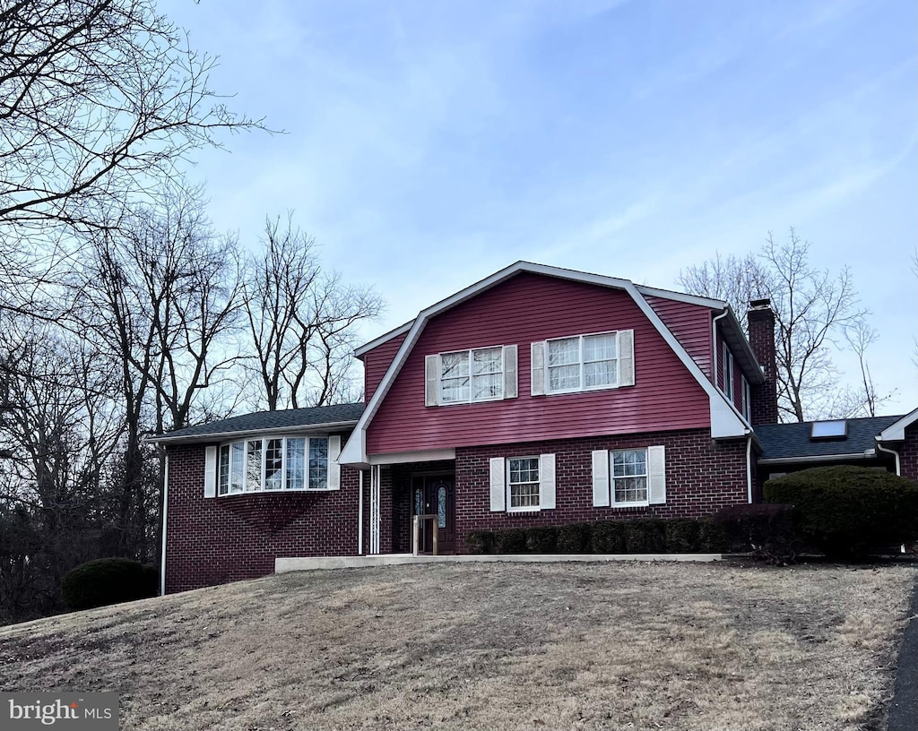 tri-level home featuring brick siding, a chimney, and a gambrel roof