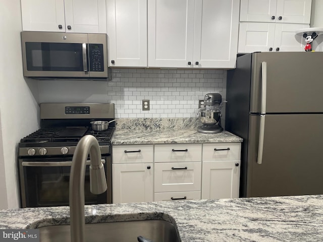 kitchen with appliances with stainless steel finishes, white cabinetry, backsplash, and light stone counters