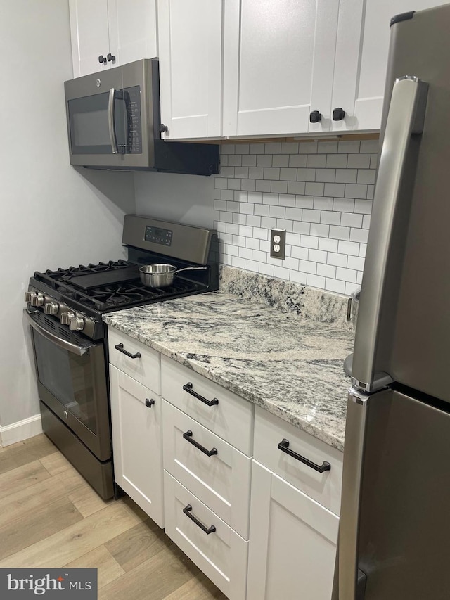 kitchen featuring light stone counters, white cabinetry, light wood-style floors, appliances with stainless steel finishes, and decorative backsplash