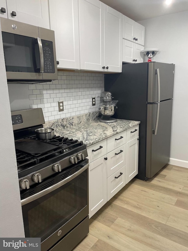 kitchen featuring stainless steel appliances, decorative backsplash, white cabinetry, and light wood-style floors