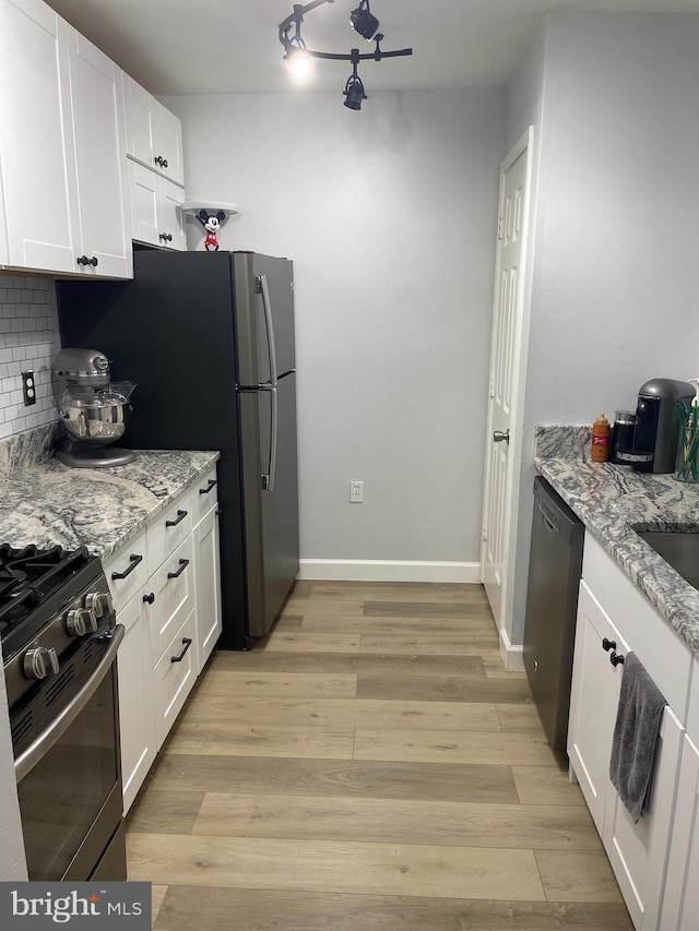 kitchen with white cabinets, light stone counters, stainless steel appliances, light wood-style floors, and backsplash