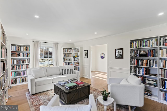 living area featuring light wood-style floors, recessed lighting, a wainscoted wall, and wall of books