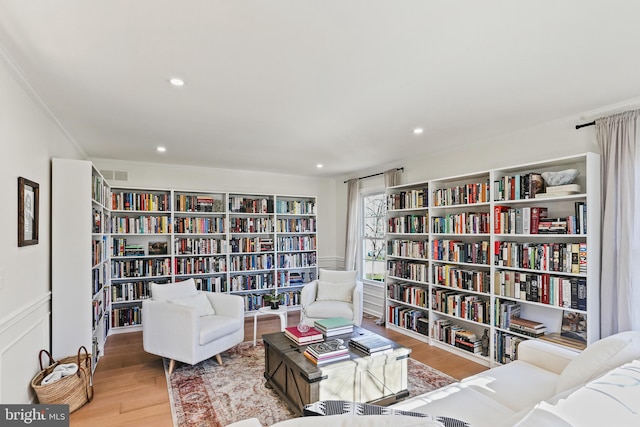 living area with ornamental molding, bookshelves, wood finished floors, and recessed lighting