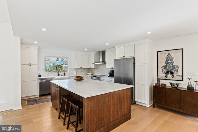 kitchen with a center island, light wood finished floors, visible vents, appliances with stainless steel finishes, and wall chimney exhaust hood